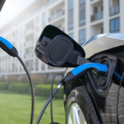 Carro elétrico preto sendo carregado em estacionamento de condomínio residencial moderno com dois cabos azuis. Carro elétrico preto sendo carregado em estacionamento de condomínio residencial moderno com dois cabos azuis.