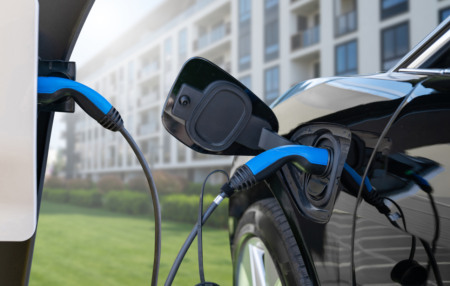 Carro elétrico preto sendo carregado em estacionamento de condomínio residencial moderno com dois cabos azuis. Carro elétrico preto sendo carregado em estacionamento de condomínio residencial moderno com dois cabos azuis.