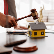 Homem bate martelo sobre mesa. Há uma miniatura de casa sobre a mesa Homem bate martelo sobre mesa. Há uma miniatura de casa sobre a mesa
