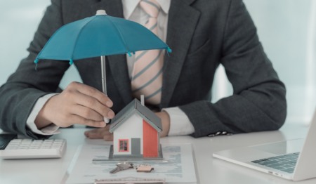 Corretor de seguros segurando um guarda-chuva azul sobre uma casa de madeira; conceito de seguro residencial/proteção e segurança do lar; seguro familiar; garantia residencial, caução ou fança, foto em close-up. Corretor de seguros segurando um guarda-chuva azul sobre uma casa de madeira; conceito de seguro residencial/proteção e segurança do lar; seguro familiar; garantia residencial, caução ou fança, foto em close-up.