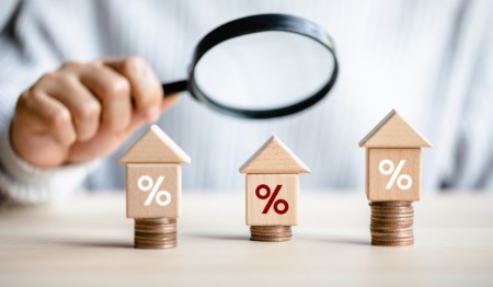 Mão segura lupa e examina três casinhas, cada uma delas em cima de moedas de dinheiro e com o símbolo de percentual (%) desenhado. Imagem representa índice de reajuste de aluguel ou qualquer outra comparação de preços relacionada ao mercado imobiliário. Foto: Pornpimone Audkamkong / iStock Mão segura lupa e examina três casinhas, cada uma delas em cima de moedas de dinheiro e com o símbolo de percentual (%) desenhado. Imagem representa índice de reajuste de aluguel ou qualquer outra comparação de preços relacionada ao mercado imobiliário. Foto: Pornpimone Audkamkong / iStock