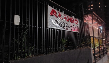 Faixa com escrito ALUGO e telefone, pregada em uma grade em frente a um imóvel. Faixa com escrito ALUGO e telefone, pregada em uma grade em frente a um imóvel.