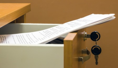 Gaveta aberta com documento (contrato de compra e venda de imóvel, por exemplo) dentro. Remete à ideia de contrato de gaveta.