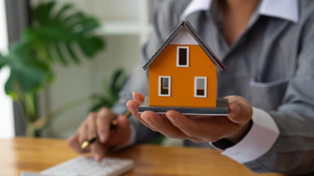Casa laranja, segurada por uma pessoa com roupa formal; entenda as regras do financiamento imobiliário Casa laranja, segurada por uma pessoa com roupa formal; entenda as regras do financiamento imobiliário