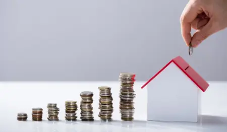 Imagem mostra pilha de moedas crescendo em direção a um cofre em formato de casa, que está sendo abastecido com mais uma moeda por uma pessoa. Remete à ideia de financiamento imobiliário, como o SFH. Imagem mostra pilha de moedas crescendo em direção a um cofre em formato de casa, que está sendo abastecido com mais uma moeda por uma pessoa. Remete à ideia de financiamento imobiliário, como o SFH.