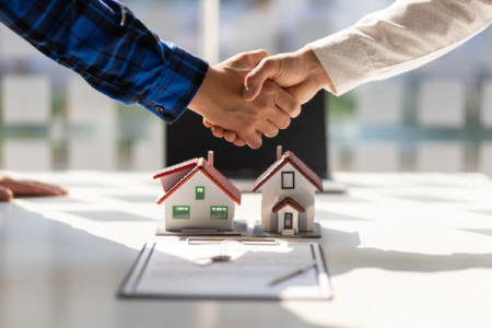 Aperto de mãos entre corretor e cliente sobre maquetes de casas e contrato de compra, simbolizando tecnologia e liderança no mercado imobiliário Aperto de mãos entre corretor e cliente sobre maquetes de casas e contrato de compra, simbolizando tecnologia e liderança no mercado imobiliário