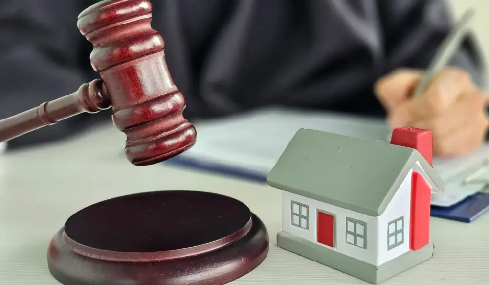 Juiz batendo martelo de leilão judicial e assinando papel, com miniatura de casa em cima da mesa, remetendo à ideia de leilão de imóveis. Juiz batendo martelo de leilão judicial e assinando papel, com miniatura de casa em cima da mesa, remetendo à ideia de leilão de imóveis.