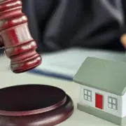 Juiz batendo martelo de leilão judicial e assinando papel, com miniatura de casa em cima da mesa, remetendo à ideia de leilão de imóveis. Juiz batendo martelo de leilão judicial e assinando papel, com miniatura de casa em cima da mesa, remetendo à ideia de leilão de imóveis.