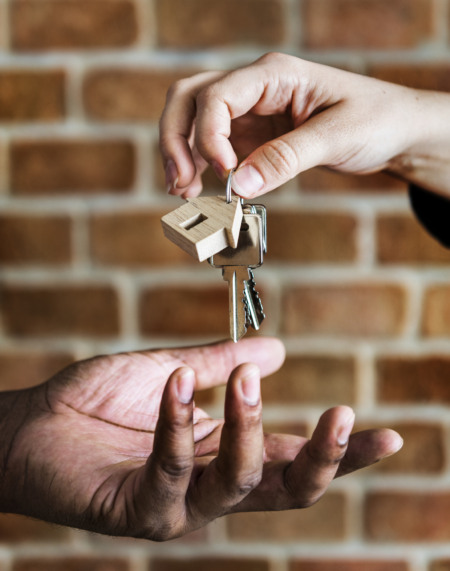 Entrega de chave de imóvel com chaveiro em formato de casa de mão em mão