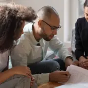 Homem verifica documentos de contrato ao lado de duas mulheres, remetendo à imagem de fiador em contrato de aluguel. Homem verifica documentos de contrato ao lado de duas mulheres, remetendo à imagem de fiador em contrato de aluguel.